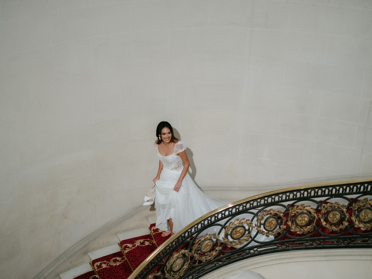bride walking down grand staircase with shoes in hand