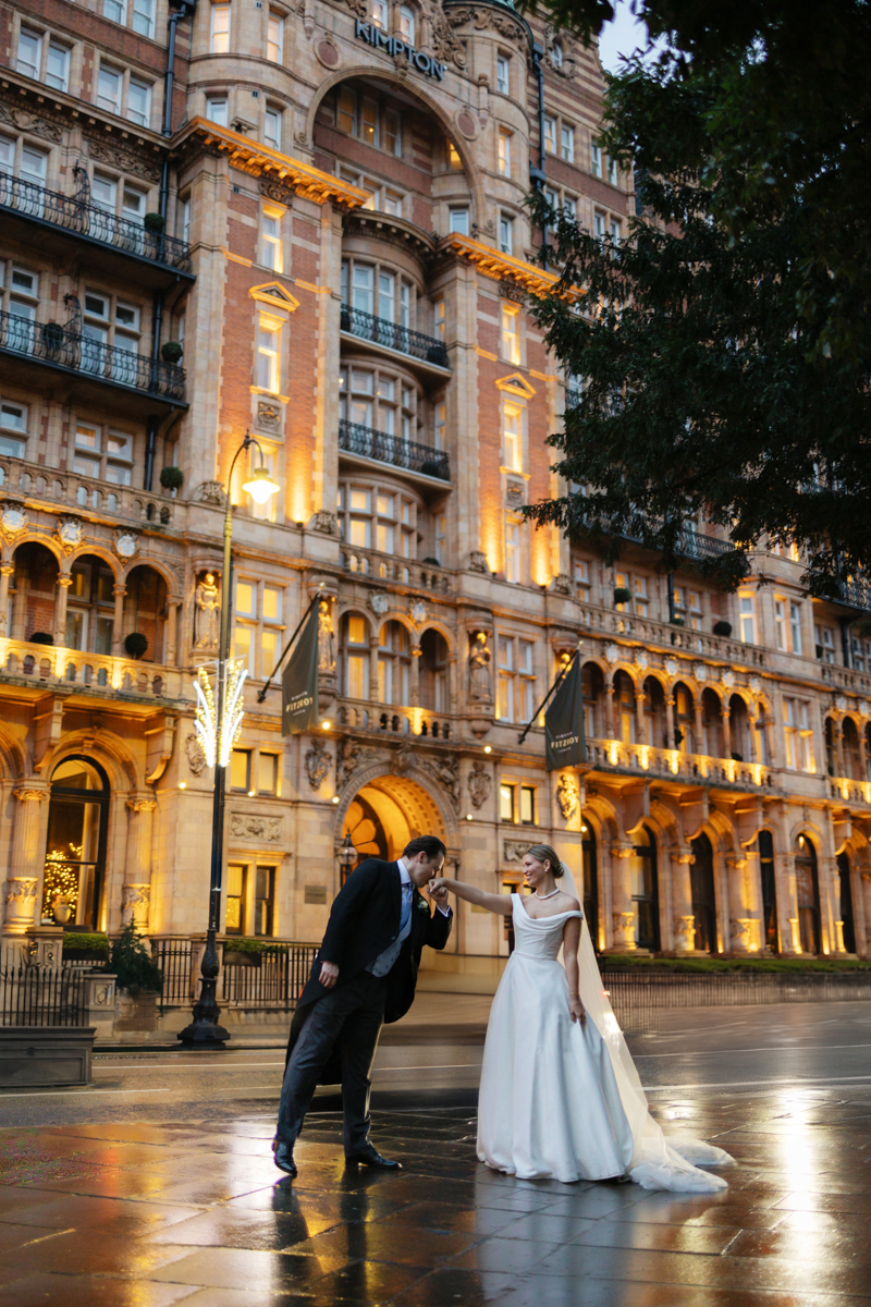 groom kissing brides hand on rainy day outside Kimpton Fitzroy